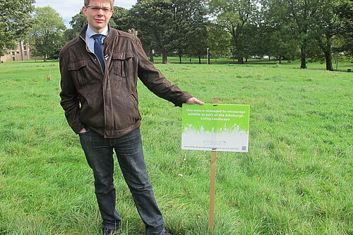 Jack Caldwell standing next to a sign in Pilrig Park that reads "this area is managed to encourage wildlife".